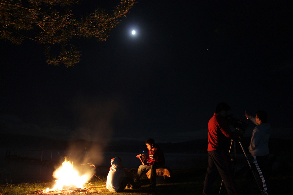 Mención honrosa 2: "Una cálida noche de verano".  Autor: Cristian Llanquileo.  "En la orilla del lago Lleu Lleu, esperaba retratar la Luna con el paisaje de fondo, junto a mis primos en primer plano (incluyéndome)". Foto tomada en enero 2016; región del Biobío.