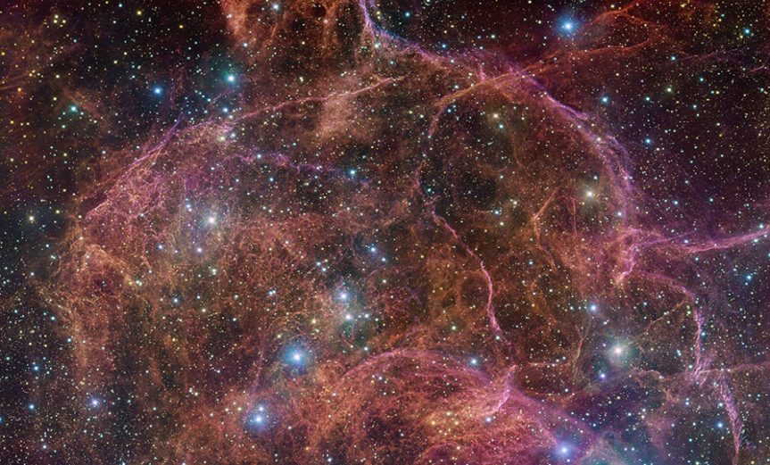 This image shows a spectacular view of the orange and pink clouds that make up what remains after the explosive death of a massive star — the Vela supernova remnant. This detailed image consists of 554 million pixels, and is a combined mosaic image of observations taken with the 268-million-pixel OmegaCAM camera at the VLT Survey Telescope, hosted at ESO’s Paranal Observatory.  OmegaCAM can take images through several filters that each let the telescope see the light emitted in a distinct colour. To capture this image, four filters have been used, represented here by a combination of magenta, blue, green and red. The result is an extremely detailed and stunning view of both the gaseous filaments in the remnant and the foreground bright blue stars that add sparkle to the image.