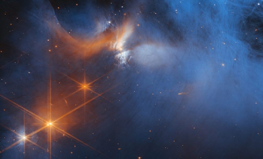 This image by the NASA/ESA/CSA James Webb Space Telescope’s Near-InfraRed Camera (NIRCam) features the central region of the Chameleon I dark molecular cloud, which resides 630 light years away. The cold, wispy cloud material (blue, centre) is illuminated in the infrared by the glow of the young, outflowing protostar Ced 110 IRS 4 (orange, upper left). The light from numerous background stars, seen as orange dots behind the cloud, can be used to detect ices in the cloud, which absorb the starlight passing through them.  An international team of astronomers has reported the discovery of diverse ices in the darkest, coldest regions of a molecular cloud measured to date by studying this region. This result allows astronomers to examine the simple icy molecules that will be incorporated into future exoplanets, while opening a new window on the origin of more complex molecules that are the first step in the creation of the building blocks of life. [Image Description: A large, dark cloud is contained within the frame. In its top half it is textured like smoke and has wispy gaps, while at the bottom and at the sides it fades gradually out of view. On the left are several orange stars: three each with six large spikes, and one behind the cloud which colours it pale blue and orange. Many tiny stars are visible, and the background is black.]